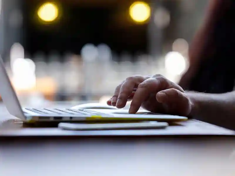 Person typing, using a laptop while seated at a wood table.